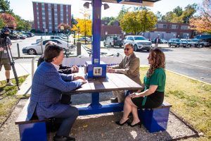 A group of people are sitting at a picnic table in a parking lot.