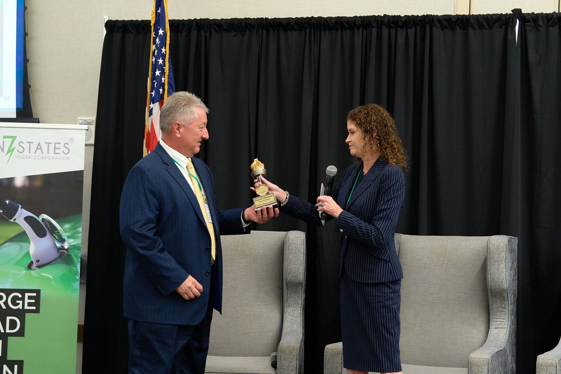 A man in a suit is giving a trophy to a woman in a suit.