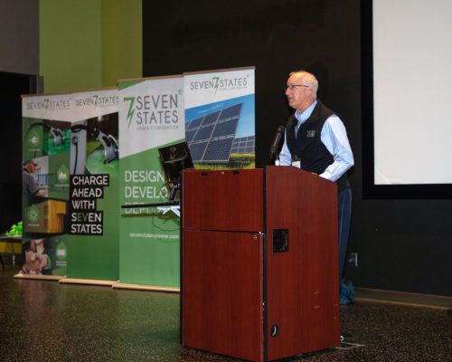 A man stands at a podium in front of a sign that says seven states