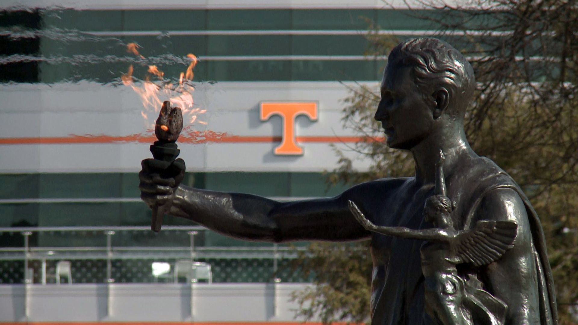 A statue of a man holding a torch in front of a building with the letter t on it.