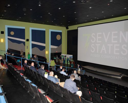 A group of people are sitting in an auditorium with seven states written on the screen