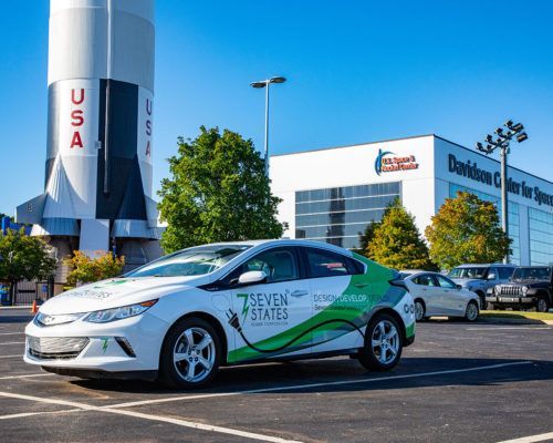 A green and white car is parked in a parking lot in front of a rocket.