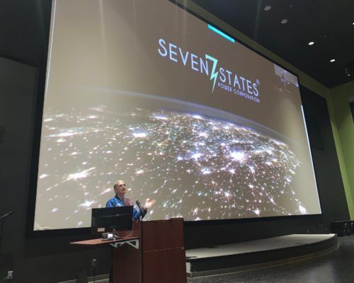 A man is giving a presentation in front of a large screen that says seven states