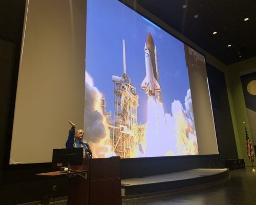A man is giving a presentation in front of a large screen
