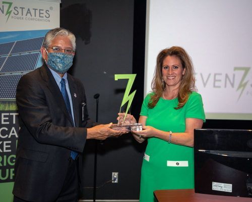 A man in a suit and tie is handing a trophy to a woman in a green dress