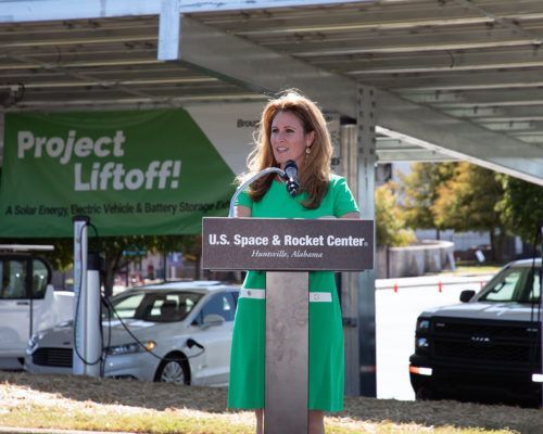A woman in a green dress stands at a podium in front of a sign that says project liftoff