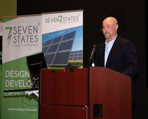 A man stands at a podium in front of a seven states sign