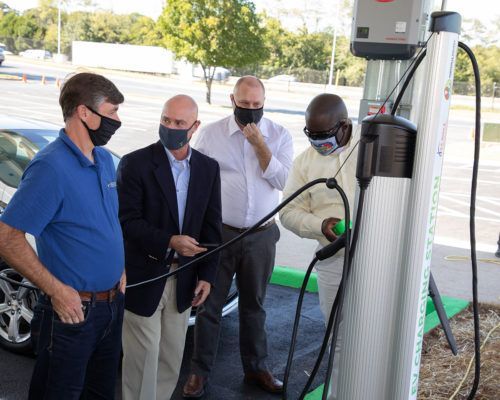 A group of men wearing face masks are standing around a charging station.