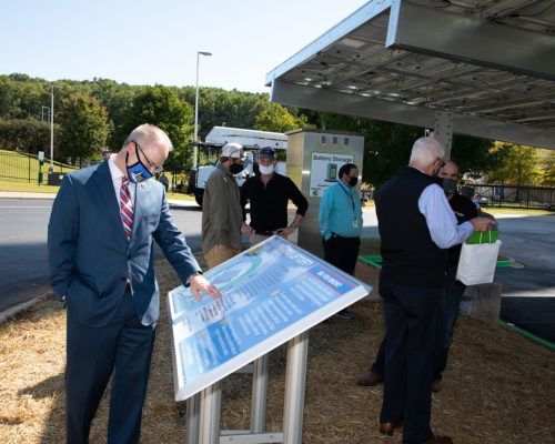 A man in a suit is pointing at a sign while standing next to a group of people.