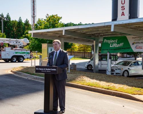 A man stands at a podium in front of a gas station that says project liftoff
