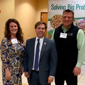 Three people are posing for a picture in front of a sign that says solving big problems.