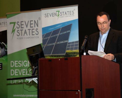 A man stands at a podium in front of a seven states sign