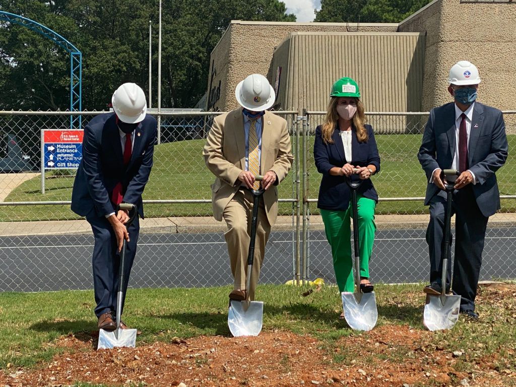 A group of people wearing hard hats and masks are digging a hole with shovels.