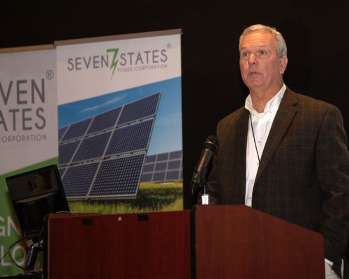 A man stands at a podium in front of a seven states sign