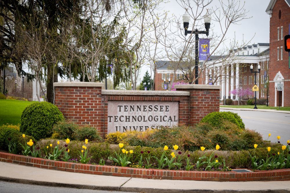 A sign for tennessee technological university is surrounded by flowers and bushes.