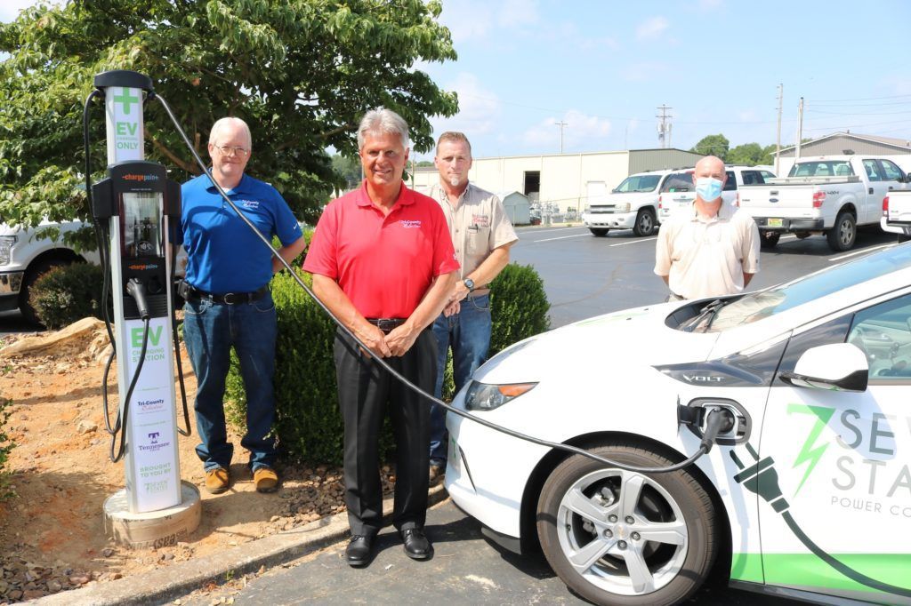 Three men are standing next to an electric car that is being charged.