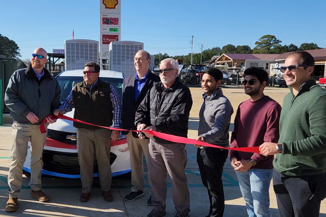 A group of men are cutting a red ribbon in front of a car.