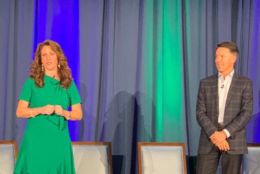 A woman in a green dress is standing next to a man in a suit on a stage.