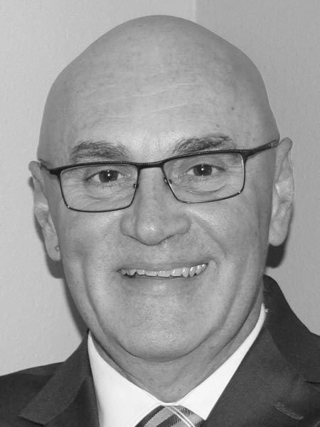 A bald man wearing glasses and a suit and tie is smiling in a black and white photo.