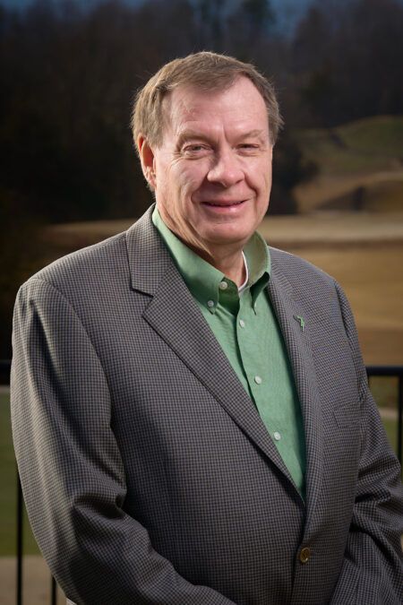A man in a suit and green shirt is smiling for the camera.