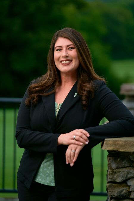 A woman in a black suit is standing next to a stone wall.