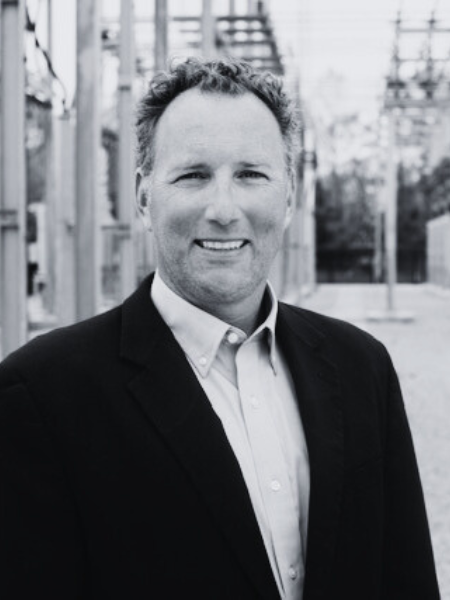 A man in a suit and white shirt is smiling in a black and white photo.