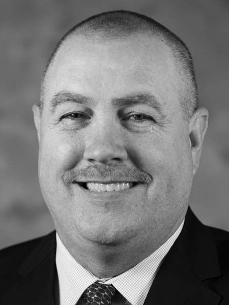 A man in a suit and tie is smiling in a black and white photo.