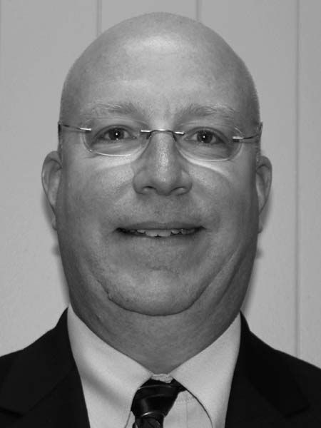 A bald man wearing glasses and a suit and tie is smiling in a black and white photo.