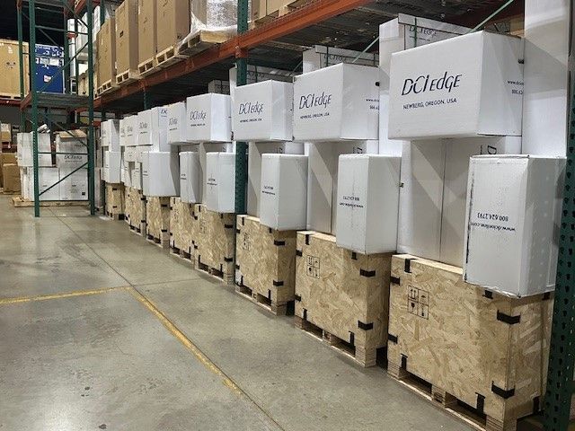 A person wearing blue gloves is holding three cardboard boxes in a warehouse.