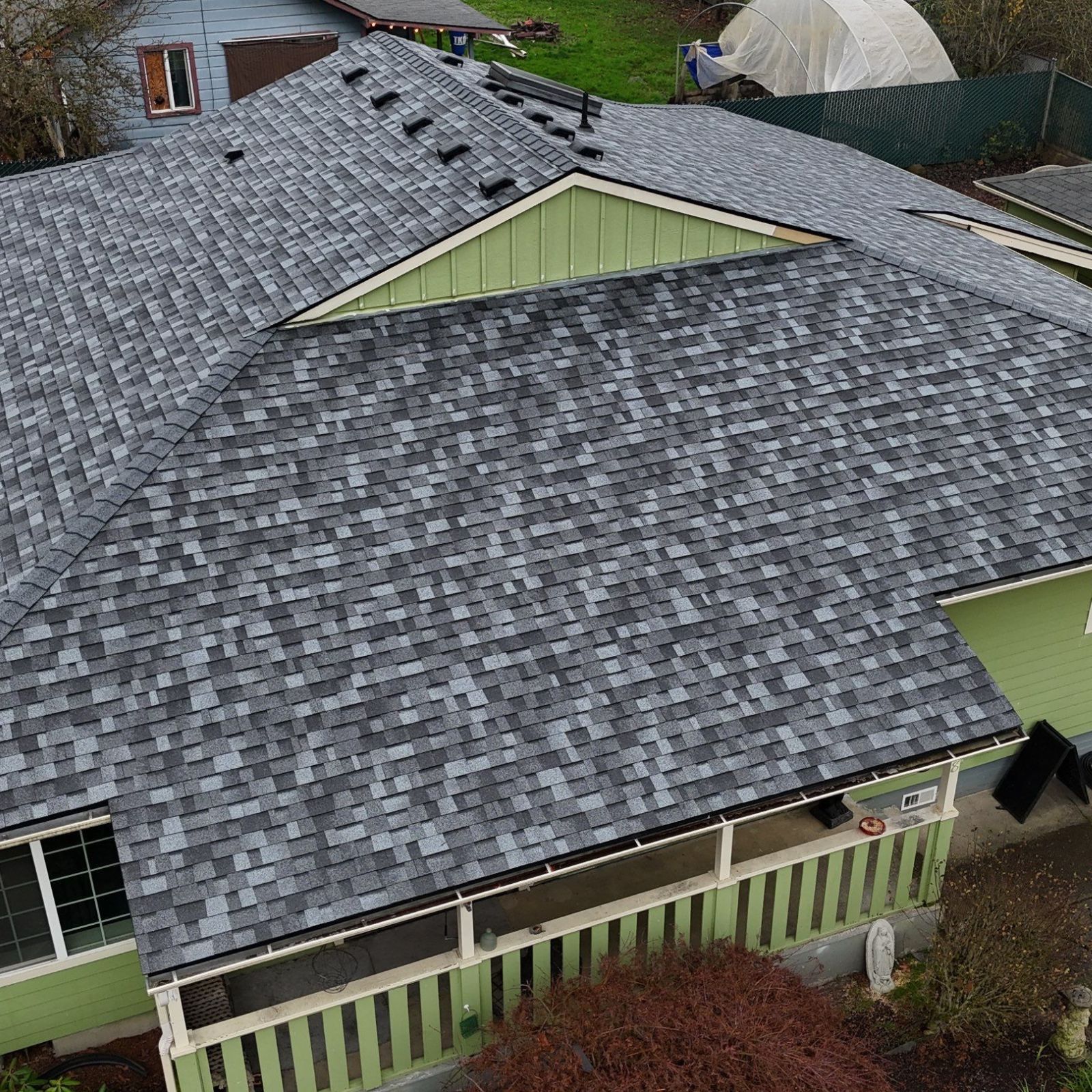 Aerial view of a house with a gray shingled roof and light green siding