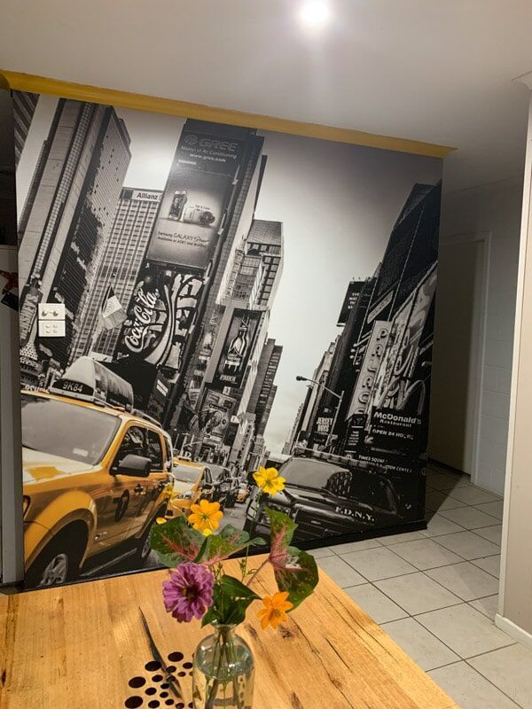 A Vase Of Flowers Sits On A Wooden Table In Front Of A Wall Mural Of A City — Cairns Signcorp In Portsmith, QLD