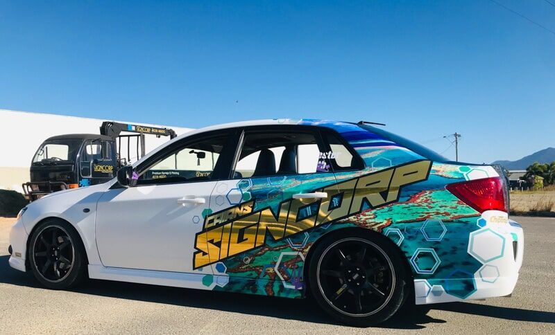A White Car With A Colourful Wrap Is Parked On The Side Of The Road — Cairns Signcorp In Portsmith, QLD