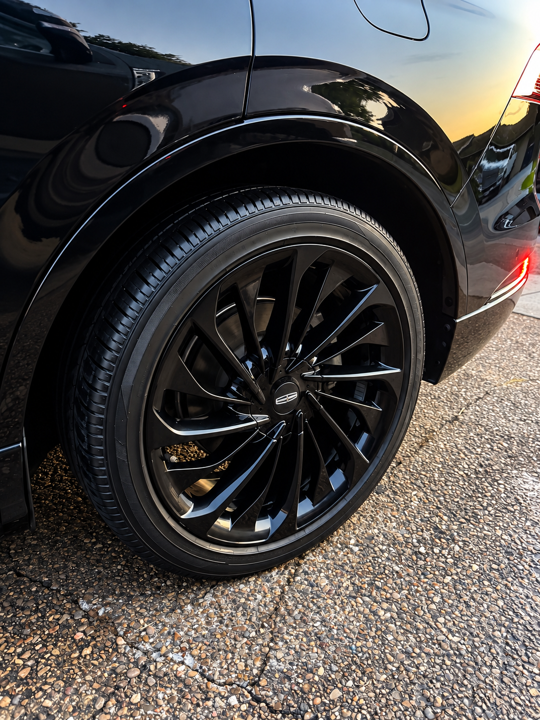 Close-up of a black car’s rear wheel with glossy black rim on wet pavement.