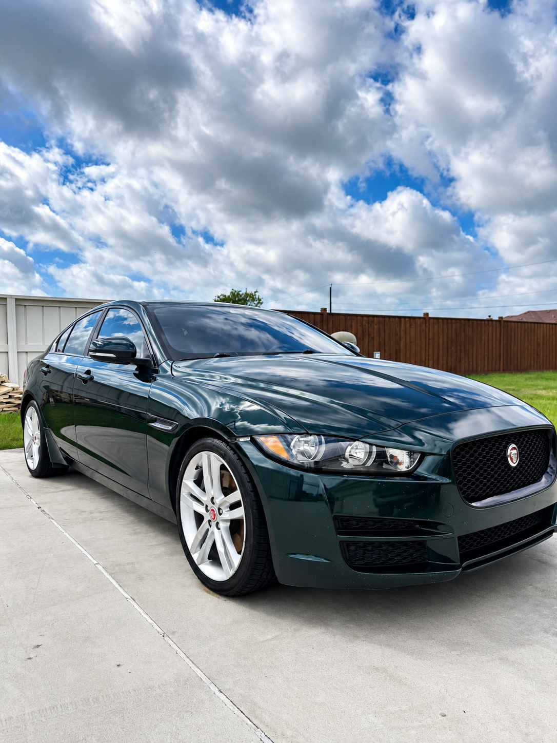Dark green sedan parked on a concrete driveway under a cloudy sky, front three-quarter view