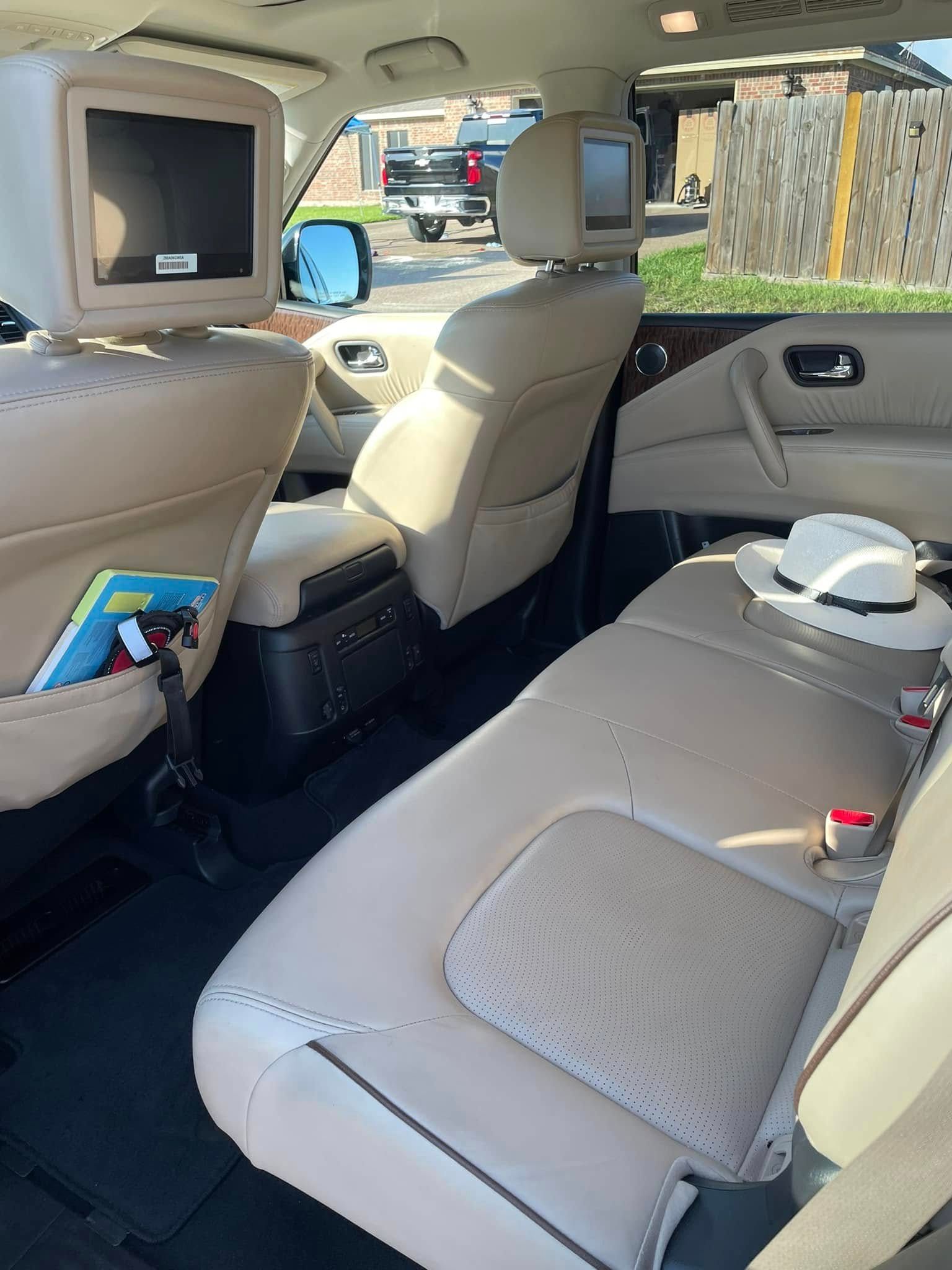 Beige SUV back seat with screens, a tablet in the seat pocket, and a cup on the center armrest.