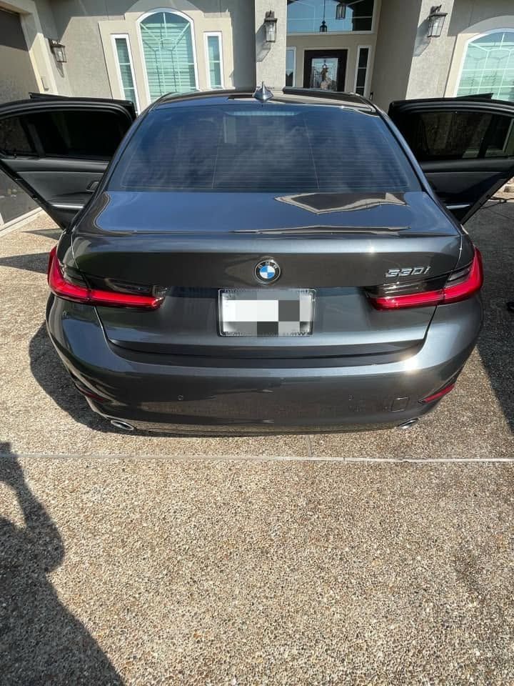 Rear view of a black BMW sedan parked in a driveway with both rear doors open.