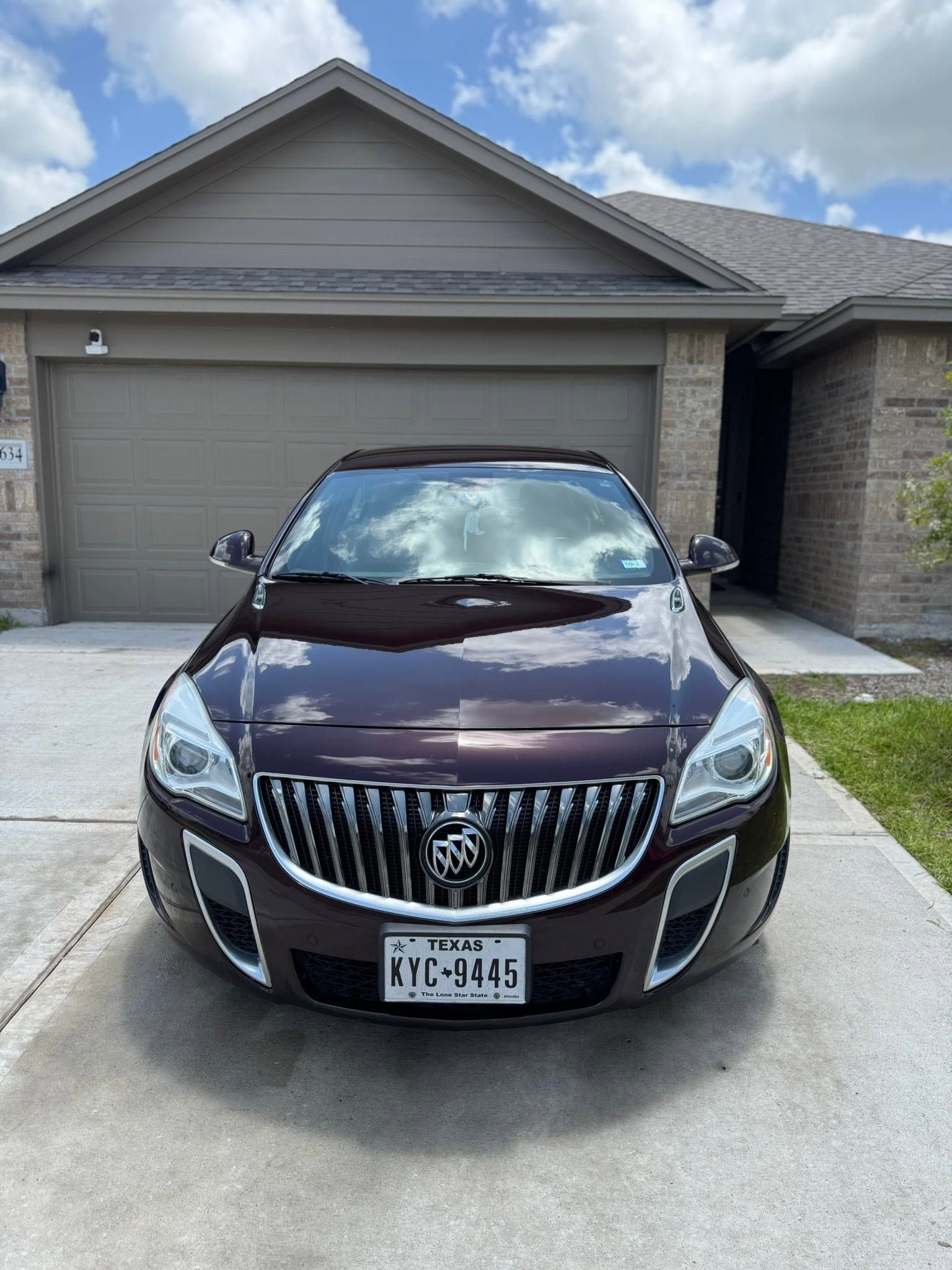 Maroon Buick sedan parked in front of a beige suburban garage under a cloudy sky