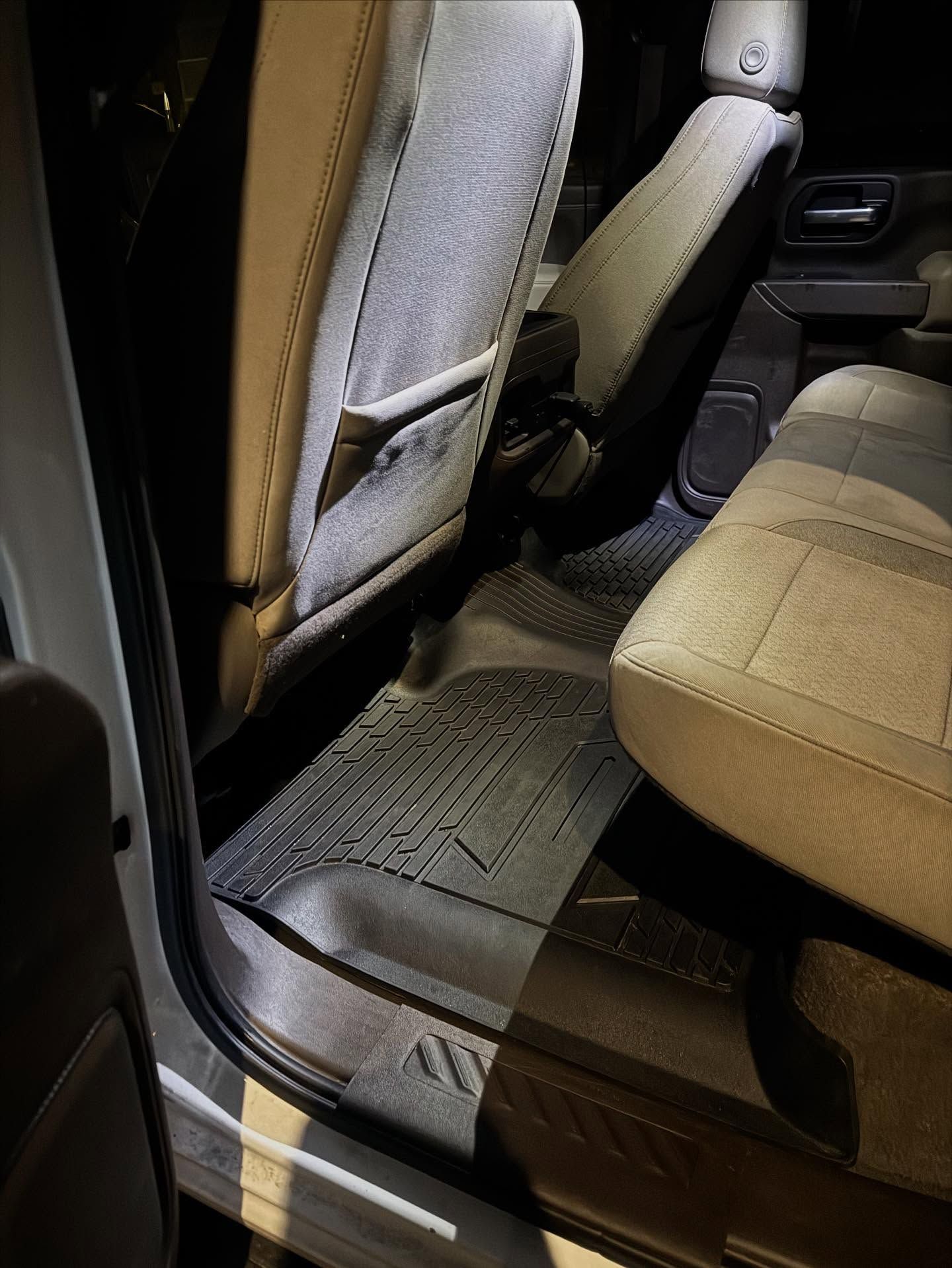Car interior with tan seats and floor mat, viewed from the rear door opening.