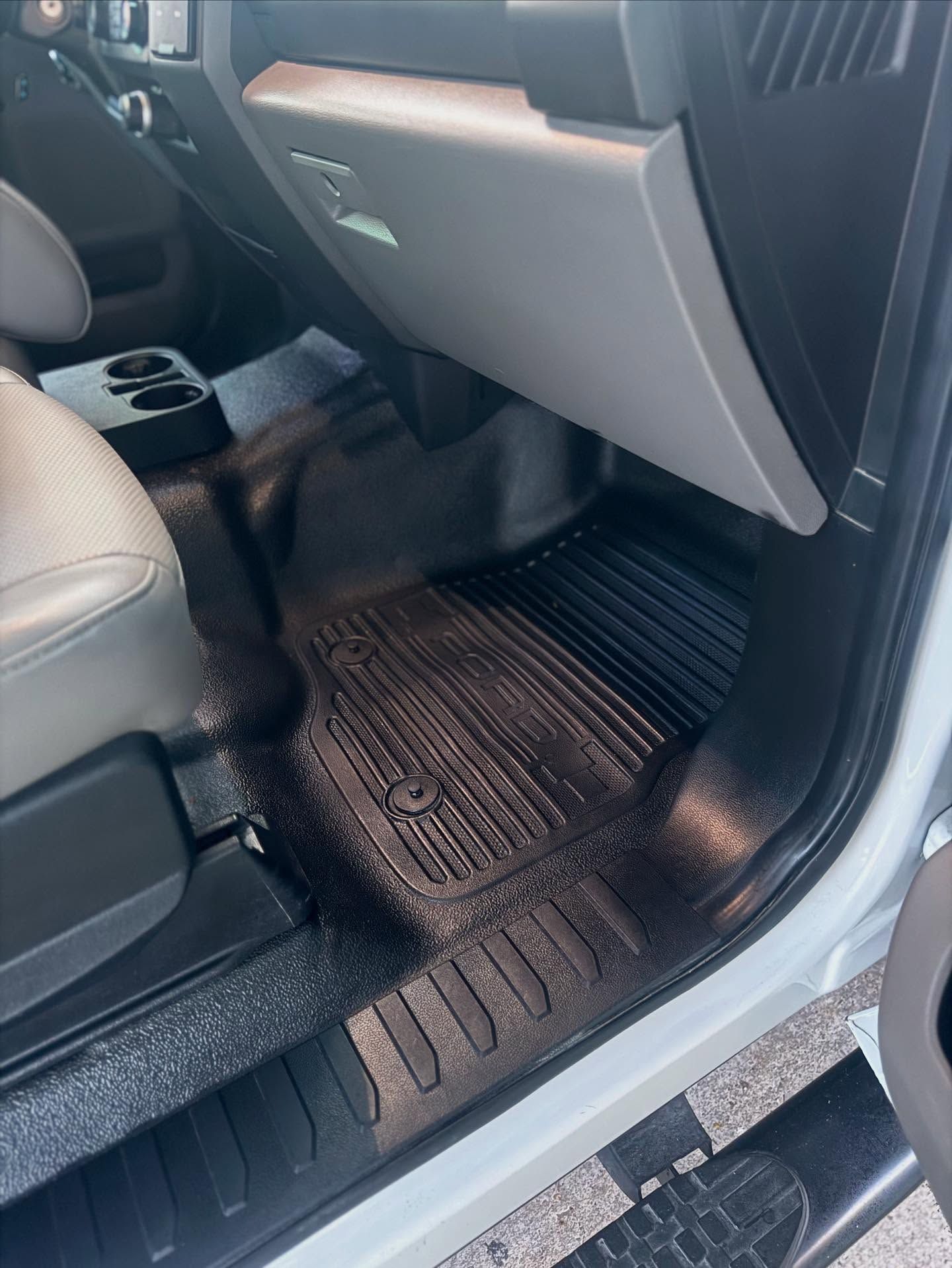 Car floor mat and footwell under the glovebox, with the door open.