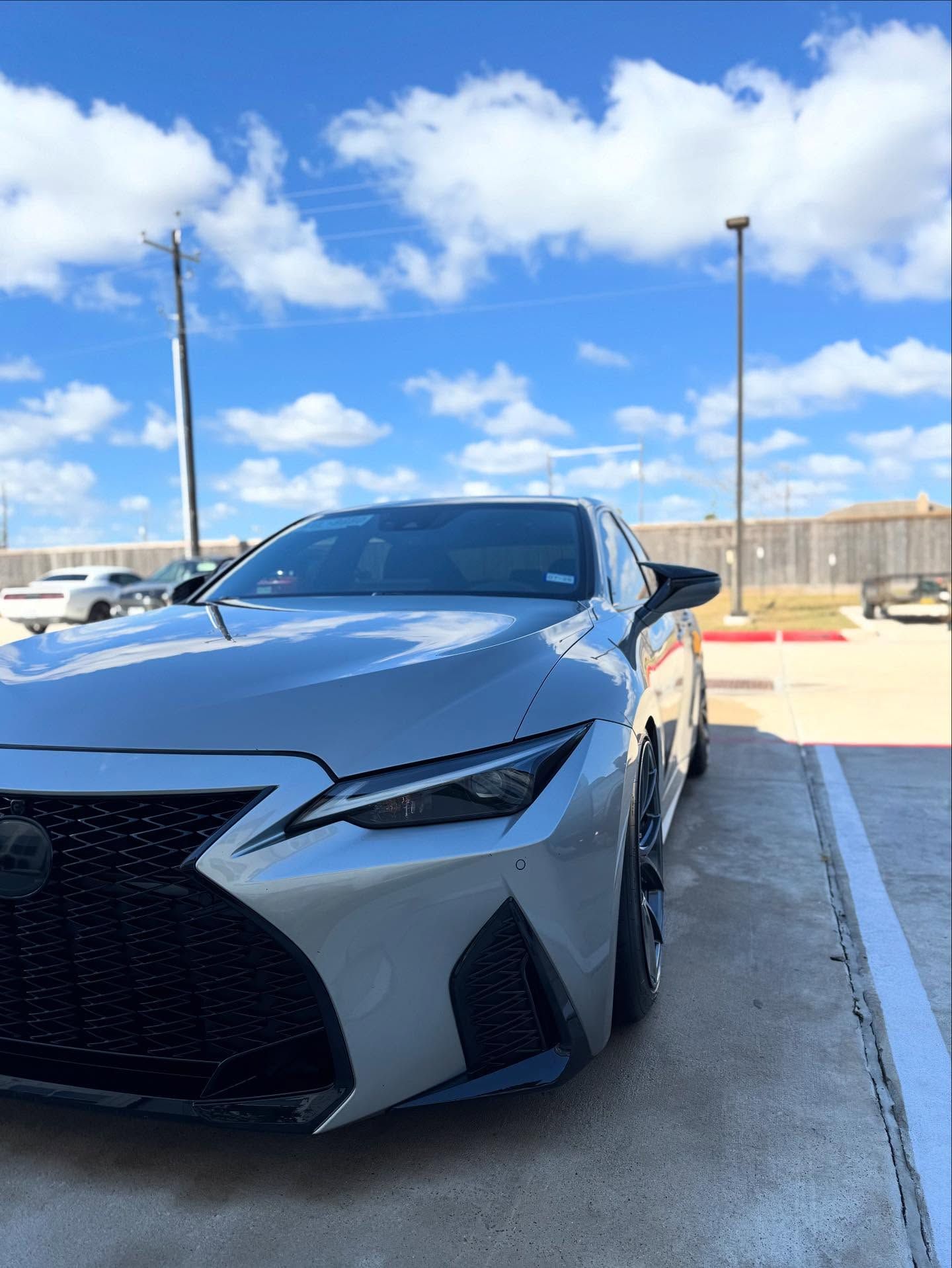 Gray sports sedan parked outdoors in a sunny lot, front-left view, with a black grille and sharp headlights