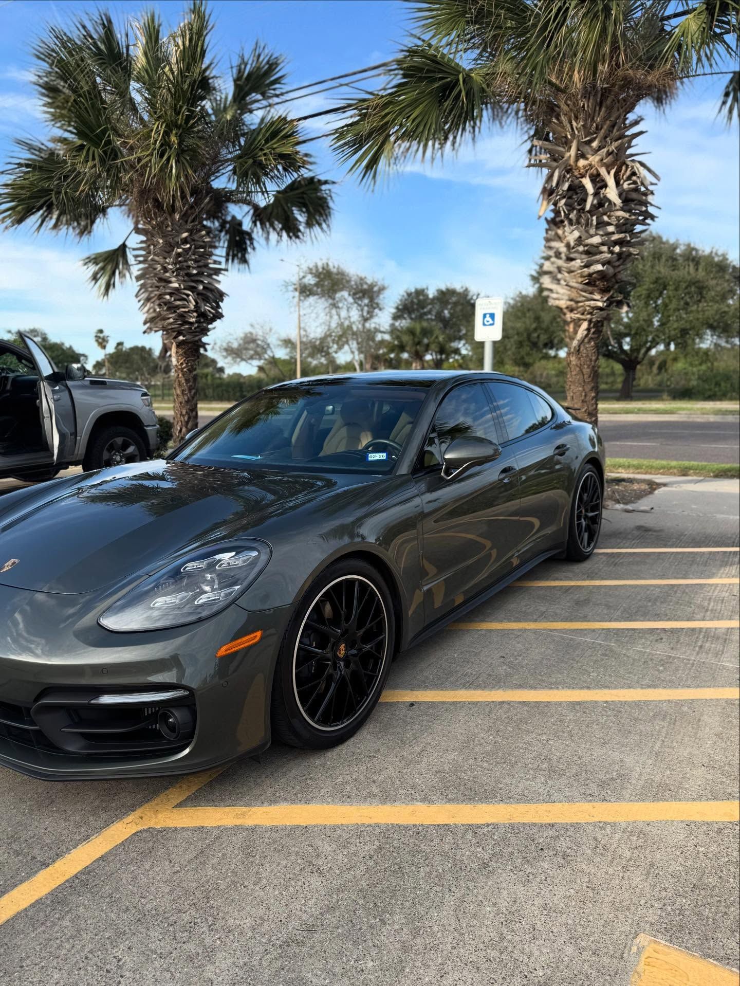 Dark gray sports sedan parked in a lot with palm trees and yellow-lined spaces.