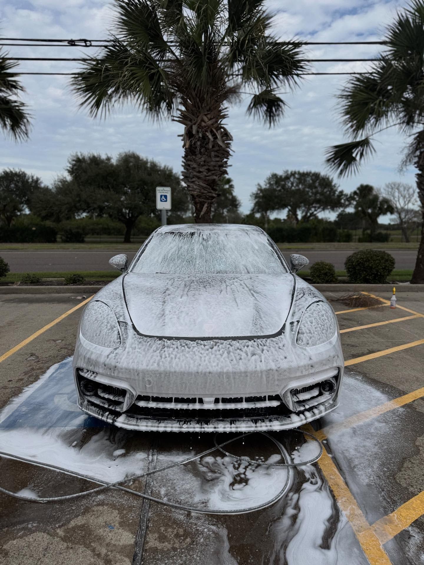 White sports car covered in foam being washed with pressure water in a parking lot