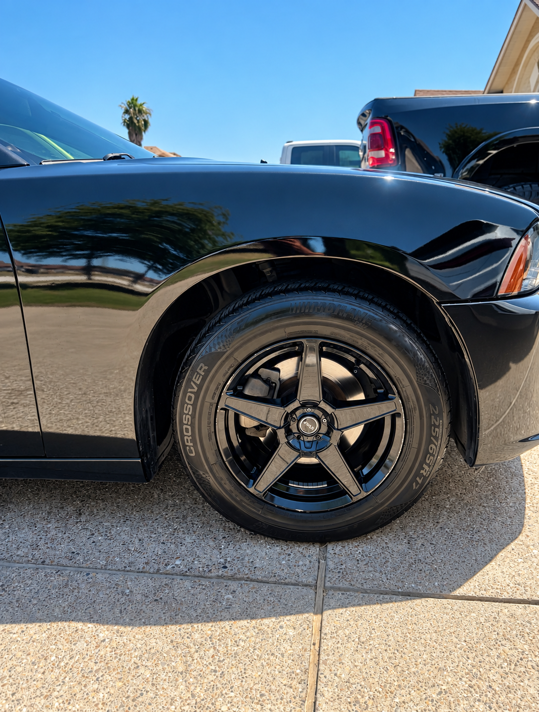 Black car front wheel and fender parked on a sunny driveway.