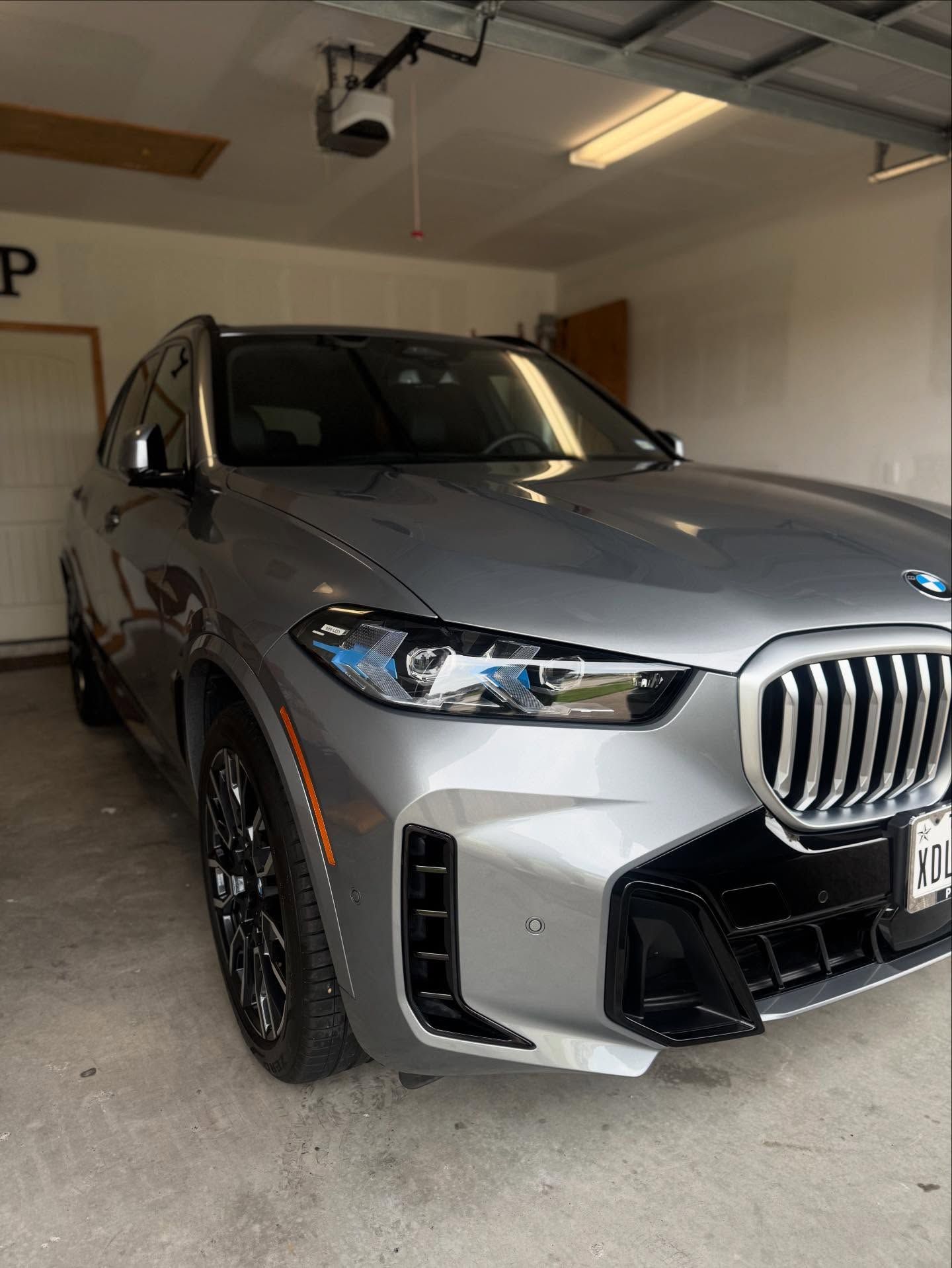 Silver BMW SUV parked in a garage, front-left view with headlights and grille visible