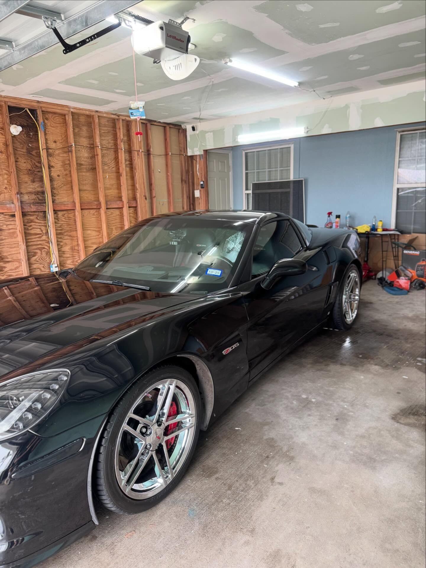 Black sports car parked in a garage with exposed wall studs and tools nearby