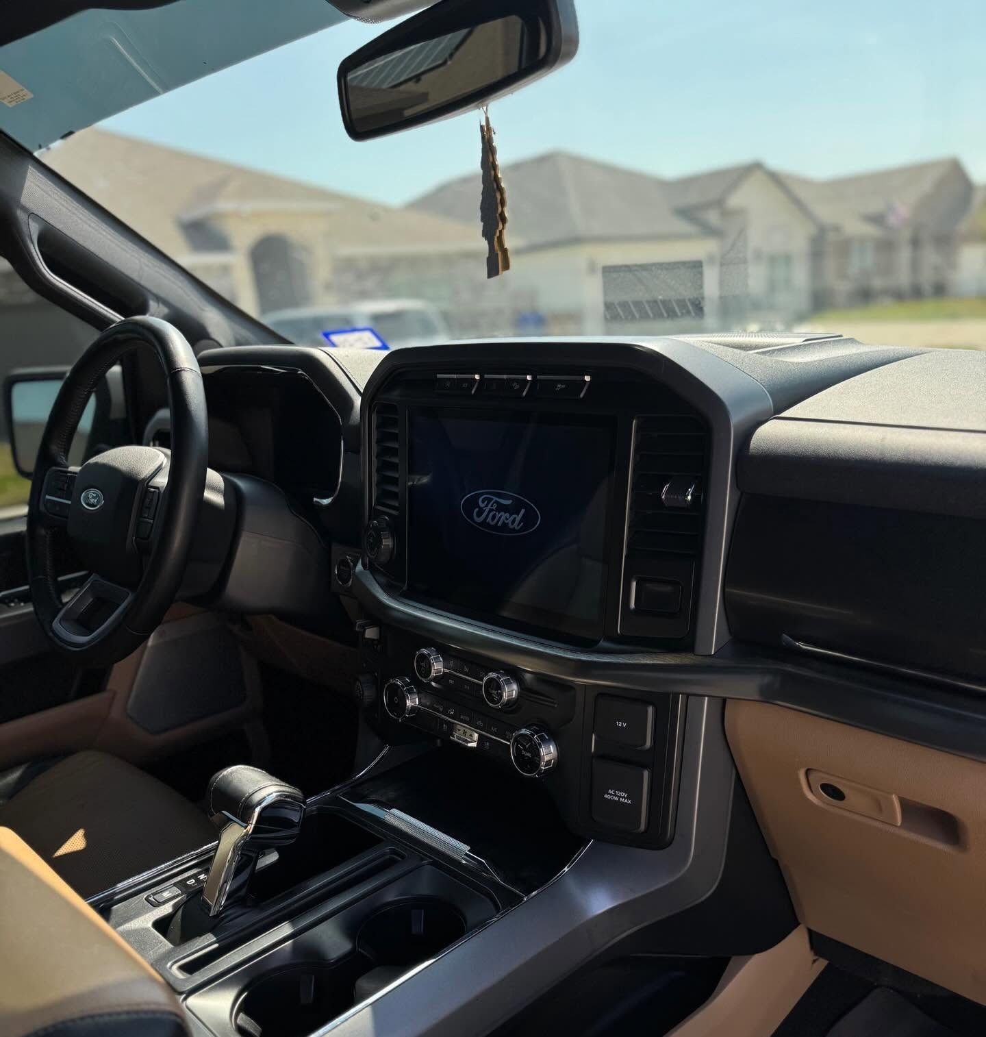 Open truck door showing black leather interior and dashboard under a bright blue sky
