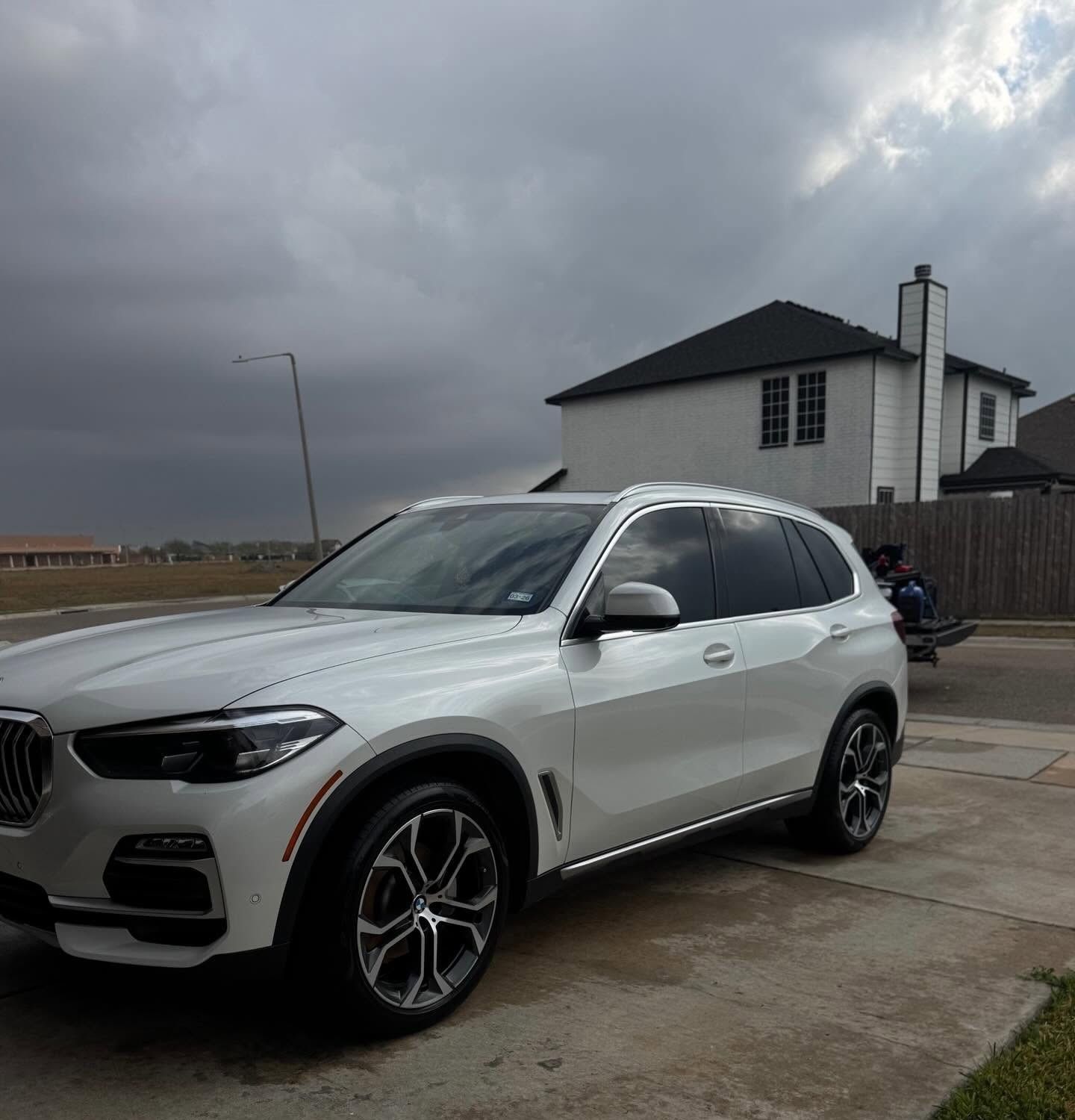 White BMW SUV parked in a driveway under a cloudy sky, beside a house