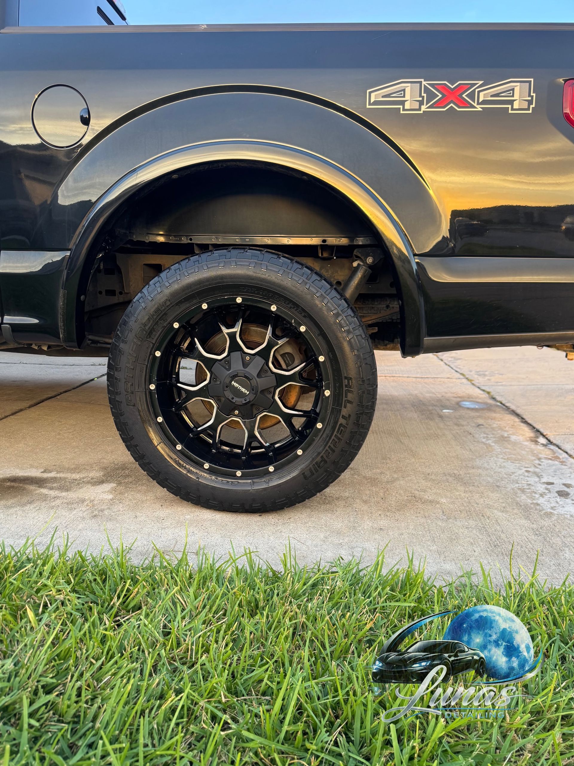 Black 4x4 truck side panel and wheel on driveway, with grass and a blue globe toy in the foreground