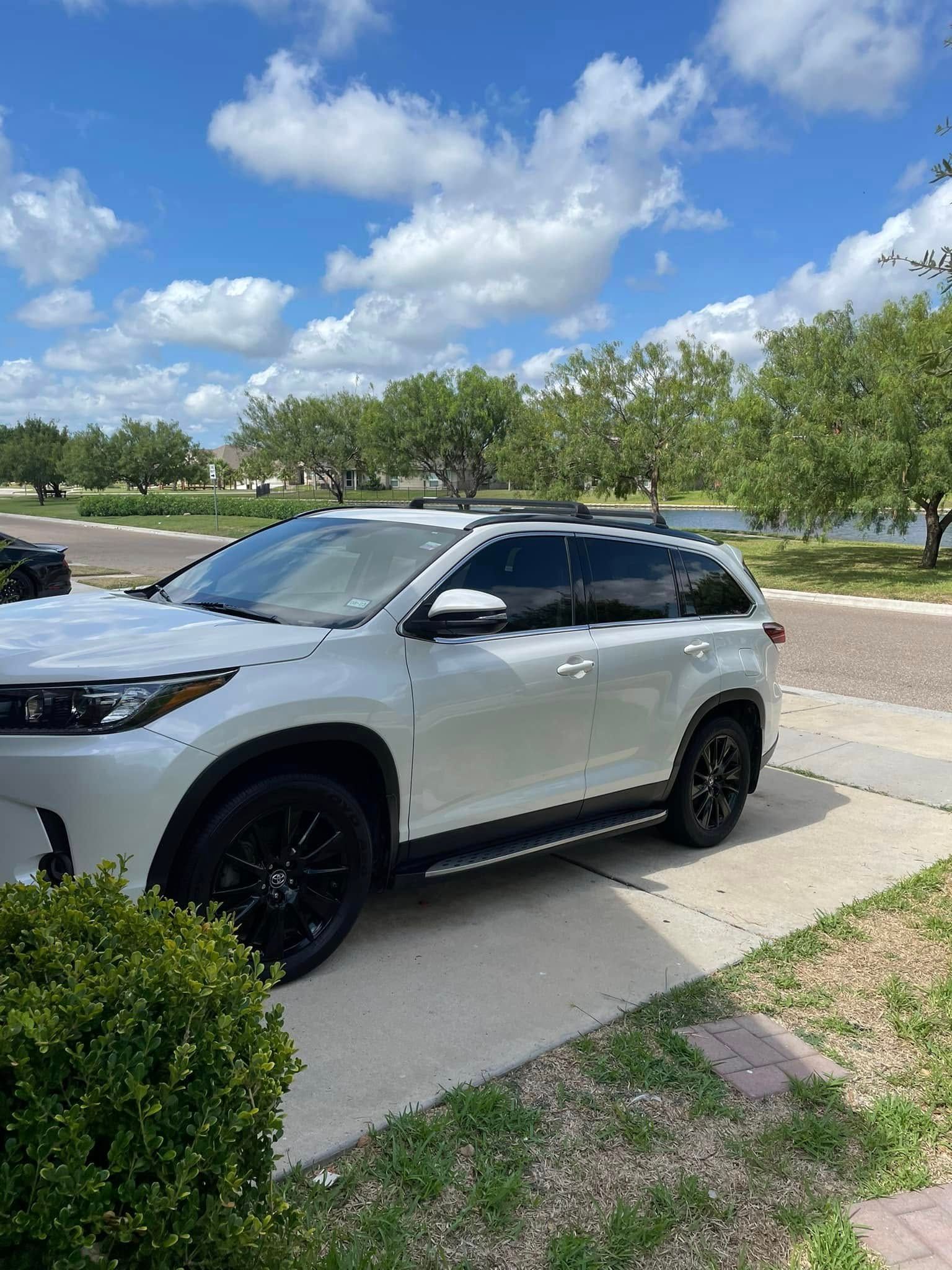 White SUV parked on a driveway beside grass and trees under a partly cloudy blue sky