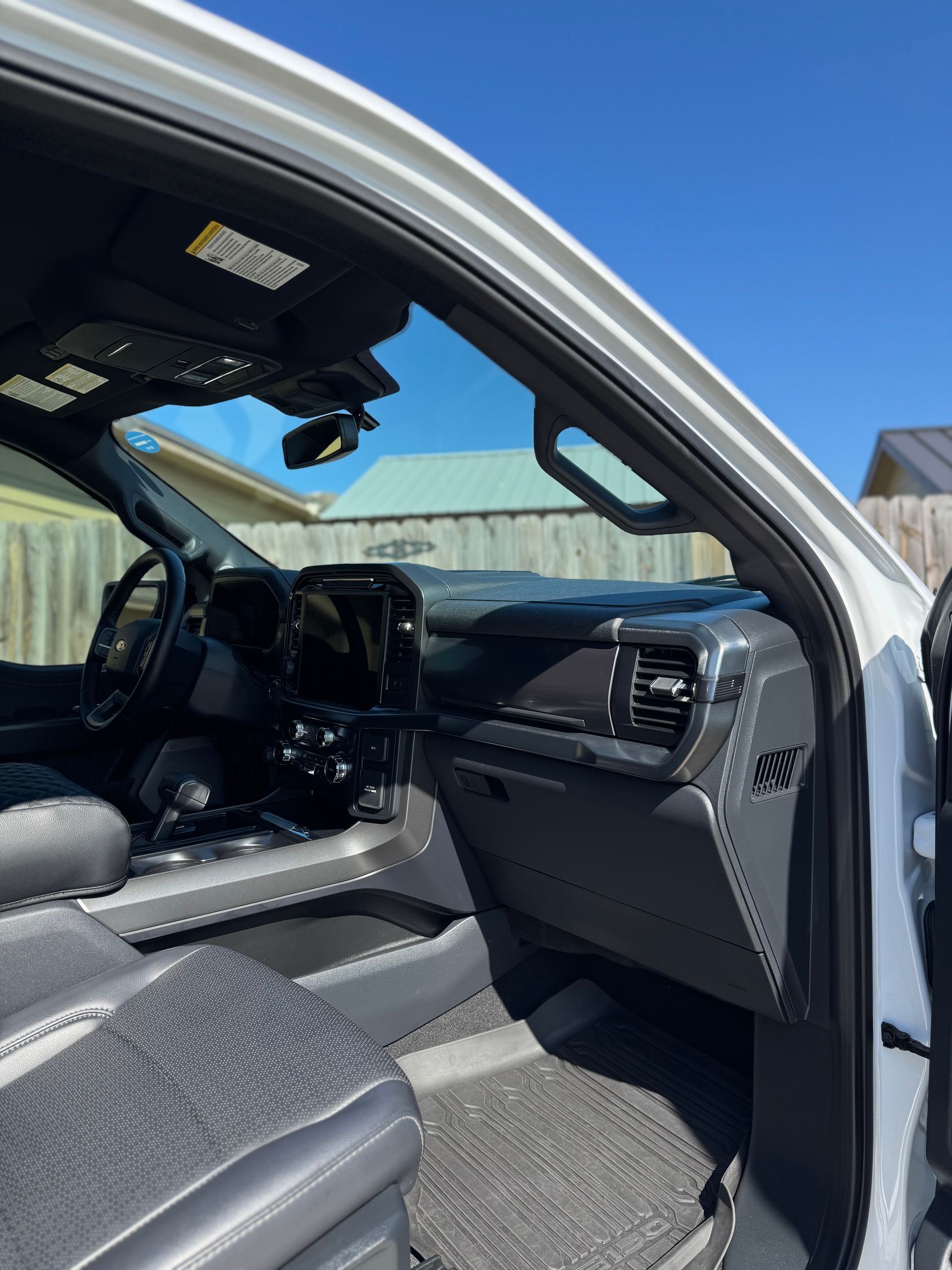 Open truck door showing black leather interior and dashboard under a bright blue sky